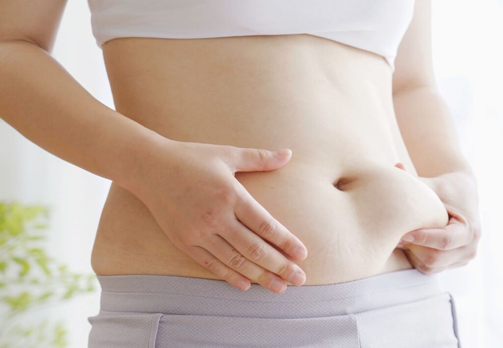 お腹を摘まむ女性